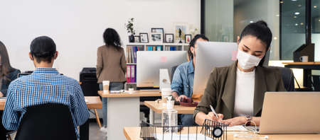 Group of Asian team business people working in office with new normal lifestyle concept. Man and woman wear protective face mask and keep distancing to prevent covid in company workplace.の写真素材