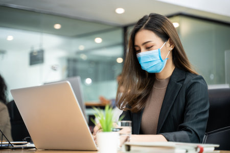 Group of Asian team business people working in office with new normal lifestyle concept. Man and woman wear protective face mask and keep distancing to prevent virus in company workplace.の写真素材