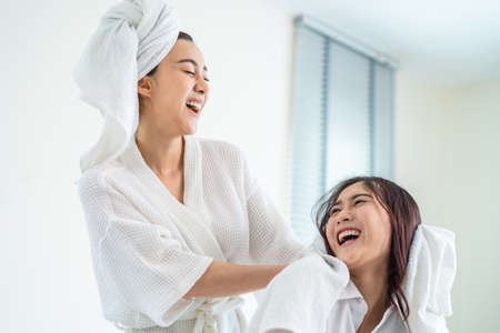Asian beautiful lesbian couple spending morning leisure time together. Attractive romantic girl in pajamas drying girlfriend's hair after shower on bed in bedroom in house. Homosexual-LGBTQ concept.の写真素材