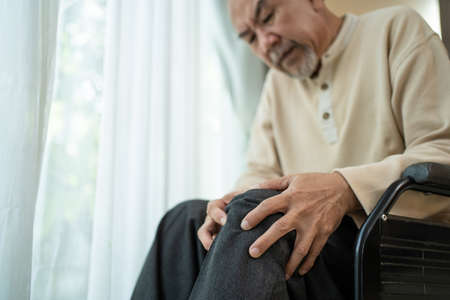 Asian Senior Elderly disabled man sit on wheelchair, suffering from injured leg at nursing home. Painful Mature Older male patient has knee problem. Hospital Insurance Healthcare and medical concept.の写真素材