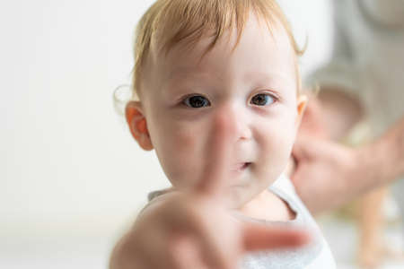 Portrait of Caucasian adorable baby boy kid smile, looking at camera. Cute little young toddler son feel happy while learn to walk on floor in house with parents support. Children development concept.の写真素材