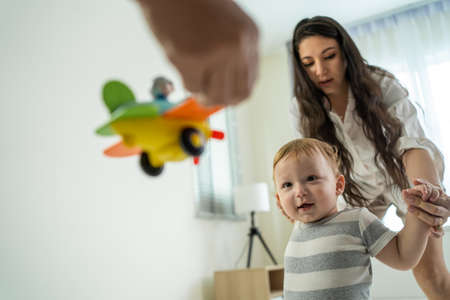 Caucasian baby boy child learn to walk with parents support in house. Happy family, mother and...