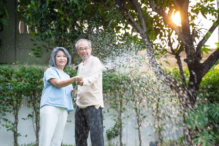 Asian Senior couple spending time outdoor gardening together at home. Attractive old grandparents use hose to watering Plants in the evening. Elderly people relationship and activity in house concept.の写真素材
