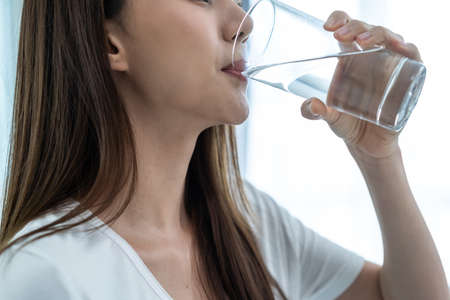 Close up of Asian attractive woman drink a glass of water in bedroom. Young thirsty beautiful girl...