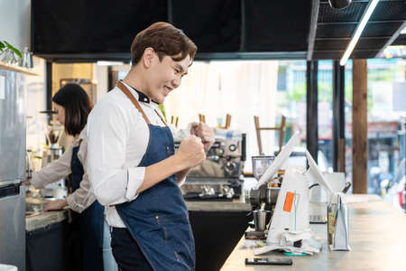 Asian cafe shop owner man check sale order from laptop on counter bar. Young attractive handsome...