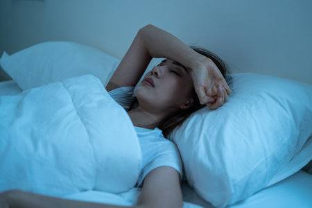 Asian frustrated girl in pajamas lying awake on bed in dark night time. Attractive beautiful depressed young woman feeling upset, worried and concerned cannot sleep from insomnia in bedroom in house.の写真素材