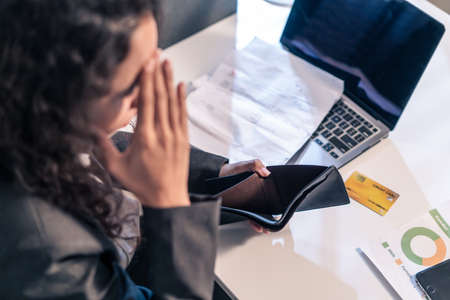 Exhausted Latino business woman hurt eye while using laptop computer. Young girl worker sitting on...