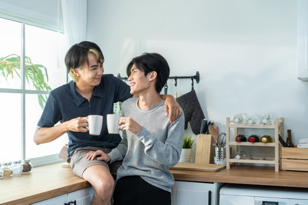 Asian man gay family sitting on counter, drink coffee for breakfast. Attractive romantic male lgbtq couple celebrate anniversary, spend time have dinner in kitchen in house. Homosexual-LGBTQ concept.の写真素材