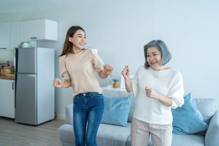 Asian funny senior old mom and daughter dance together in living room. Attractive beautiful woman and mature grandma feel happy to spend leisure time at home, enjoy listen to music on weekend in houseの写真素材