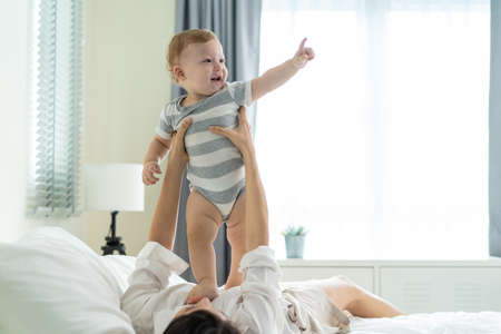 Caucasian loving mom play with cute baby boy child on bed in bedroom. Happy family, attractive...