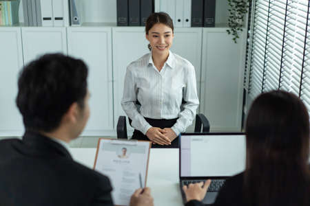 Asian beautiful woman talk with hr manager for job interview in office. Attractive female sit on table and give resume to human resources managers business recruit people for apply job at workplace.の写真素材