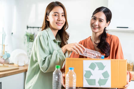 Asian beautiful woman friend separate trash for recycling at home together. Attractive lesbian couple put plastic bottles into recycle box for ecologically friendly and saving environment zero waste.の写真素材
