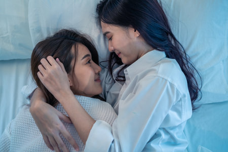 Asian beautiful lesbian couple lying down on bed and hugging each other. Attractive romantic girl friend in pajamas spending night leisure time together in bedroom in house. Homosexual-LGBTQ conceptの写真素材