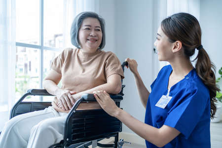 Asian nurse take care senior woman on wheelchair at nursing home care. Attractive happy Caregiver girl doctor take care older elder mature disabled patient female to window in hospital ward to look ouの写真素材