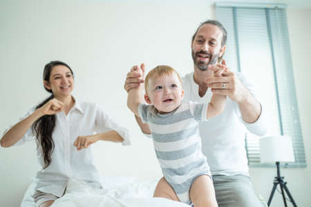Caucasian loving parents play with baby boy child on bed in bedroom. Happy family, attractive...