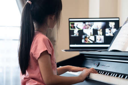 Homeschool Asian little young kid girl learning piano from computer connecting to internet music...