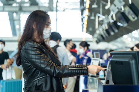 Asian female traveler giving passport to customer check in officer at airline service counter. Woman wearing face mask when traveling by airplane transportation to prevent covid19 virus pandemic.の写真素材