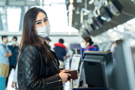 Asian female traveler holding passport at customer check in of airline service counter. New normal,...