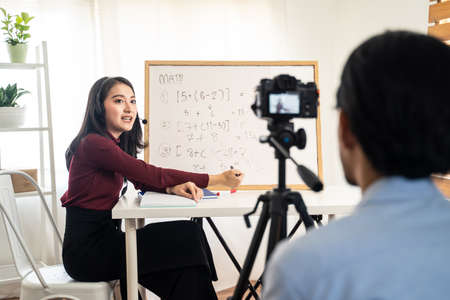 Asian school woman teacher working from home teaching online internet class to student studying from home. Man using camera to record girl digital live.の写真素材