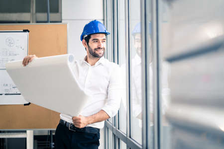 Caucasian young engineer home building member smile with new project planning while hold paper. The man hold blueprint of structure control in meeting room. Structure analysis home building concept.の写真素材