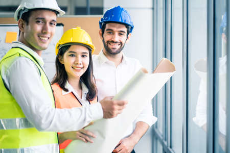 Young engineer group of home building member discuss for project planning. Asian man hold blueprint drawing while all team members look project area. People brainstorm teamwork for idea of structure.の写真素材