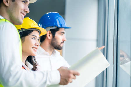 Young engineer group of home building member discuss for project planning. Asian man hold blueprint drawing while all team members look project area. People brainstorm teamwork for idea of structure.の写真素材