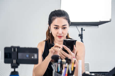 Asian young beauty cosmetic blogger woman use tablet for prepare information before record clip video about demonstrating make up techniques and informing customers about product detail at studio.の写真素材