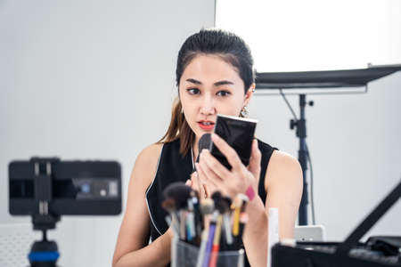 Asian young beauty cosmetic blogger woman use tablet for prepare information before record clip video about demonstrating make up techniques and informing customers about product detail at studio.の写真素材