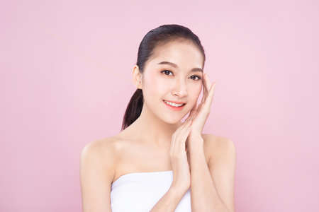 Beautiful Young Asian woman with clean fresh white skin touching her own face softly in beauty pose. Girl touching with fingers in pink background. Facial treatment, cosmetology, spa, make up concept.の写真素材