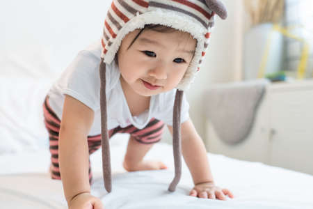 Asian little young cute baby kid lying and crawling on white bed in bedroom at home. The little...