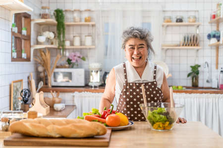 Senior Asian elder woman happy living in home kitchen. Grandmother cooking salad dish standing at counter with happiness and smile enjoy retirement life. Older people activity in family at home.の写真素材