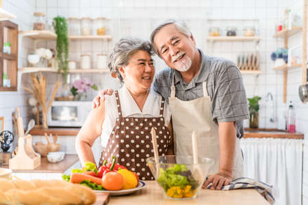 Couple senior Asian elder happy living in home kitchen. Grandfather cooking salad dish with grandmother with happiness and smile enjoy retirement life together. Older people relationship and activity.の写真素材