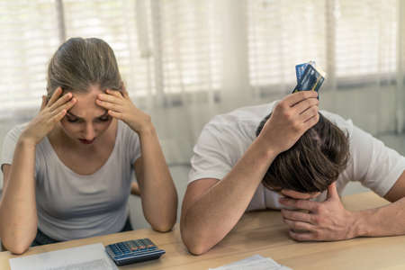 Stressed young Caucasian couples sitting with hand holding credit cards and look at bills worry about find money to pay credit card debt and all loan bills. They feel stressful. Financial problem.の写真素材