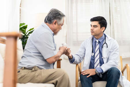 Asian senior old man with bad condition feeling sick sitting on sofa having medical check up by doctor visiting at home. Elder man getting medicine from doctor and receiving health care advisory.の写真素材