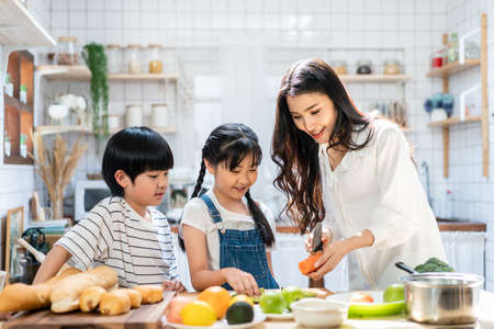 Lovely cute Asian family playing, making food in kitchen at home. Portrait of smiling mother and children standing at cooking counter that food ingredient put on table. Happy family activity together.の写真素材