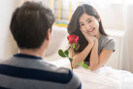 Asian young man giving red rose flower to pretty woman. Girl receiving lovely Valentine present...