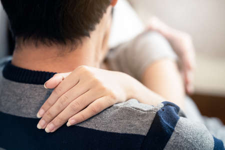 Young Asian couple sitting on bed in bedroom together. Girl holding boy shoulder and kissing. Seen from behind man and focus on woman hand, no face see. Love relationship of girl and boy concept.の写真素材