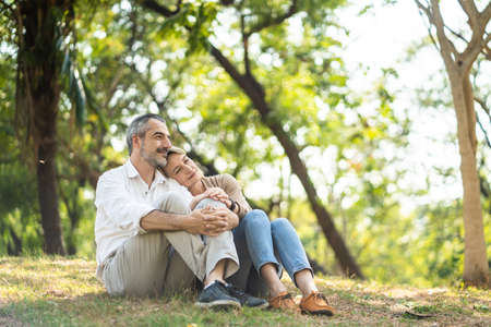 Senior elder Caucasian couple sitting on ground together in park in Autumn. Wife resting head on husband shoulder and put hands on man knee. Beautiful love relation and care of retirement old people.の写真素材