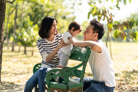 Asian family resting and relax in park together. Mother holding baby on armchair while father...