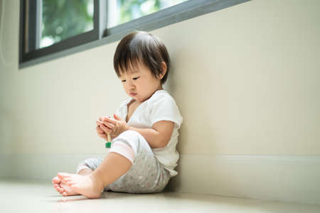 Asian cute baby sitting and playing a small toy sitting alone on floor at home. The kid holding the toy and question about how to play it. Play and learn of young child education conceptの写真素材