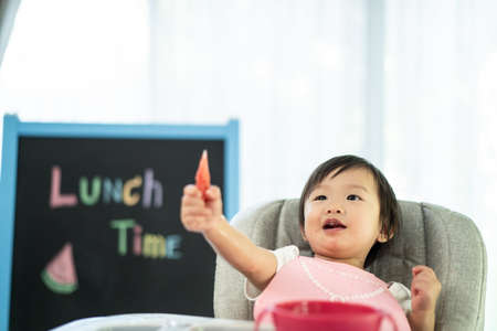 Young cute kid on baby high chair feeding seat holding watermelon with smile face at home. The child...