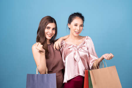 Young pretty cute two Asian woman holding shopping bags in both hands with smiley face standing in...