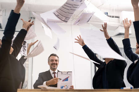 Group of diversity working people in office meeting room feeling glad and happy of achievements after their boss announce succeed result. They lifting the working paper and throw it away with smile.の写真素材