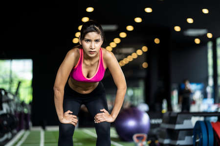 Asian beautiful sporty fit young woman feeling tired standing in Gym or fitness club after she had a hard work out. The girl exhausted expression on her face. Fitness for health concept.の写真素材