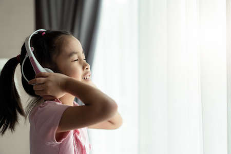 Asian cute little girl using headset listening music in the room. The kid enjoy the song feeling...