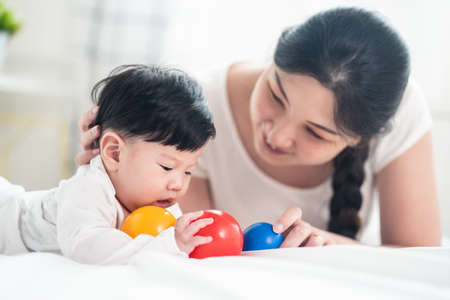 Asian young mother look at baby, hold son feet and kiss with warm love while cute boy close his eyes...