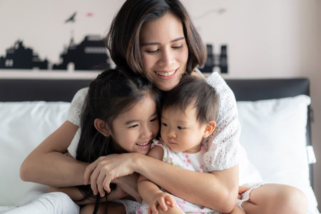 Happy Asian family activity concept. Beautiful mother hugging her children with smile sitting on bed...