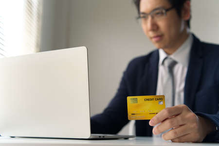 Smart handsome young business man holding dummy credit card and typing on laptop paying or shopping...
