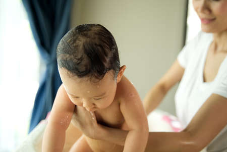 Asian beautiful mother holding little cute baby just after taking a bath her child in bathtub in the...