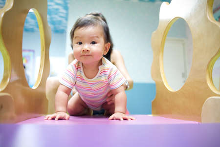 Young little smiling Asian baby enjoy playing in kid playground. Mother holding baby from her back to play on slider with happiness. Baby learning and education concept.の写真素材